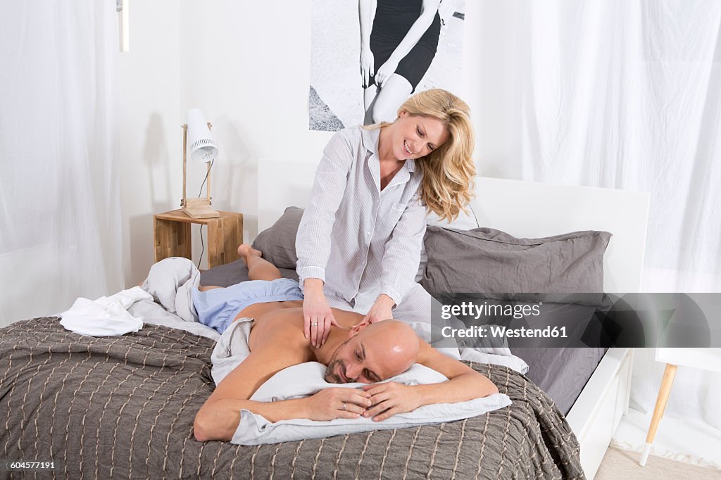 Happy couple in bedroom, woman giving man a back massage