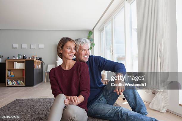 smiling couple sitting on the floor at home watching something - mirada de reojo fotografías e imágenes de stock