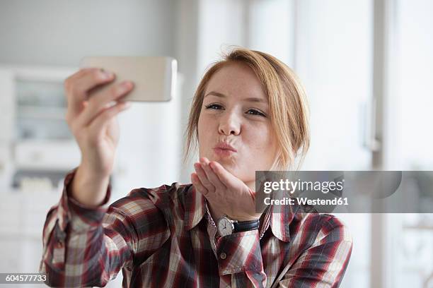 young woman blowing a kiss while taking a selfie with her smartphone - blowing a kiss stock pictures, royalty-free photos & images