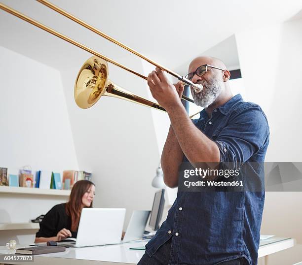 man playing trombone at home office - trombone stock pictures, royalty-free photos & images