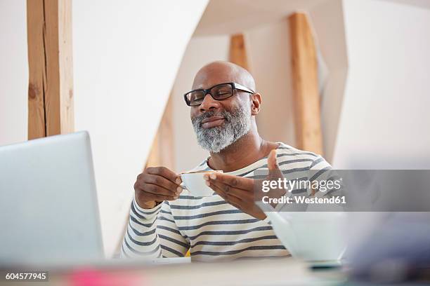 portrait of smiling man with closed eyes sitting at his desk with cup of tea - man smiling eyes closed stock pictures, royalty-free photos & images