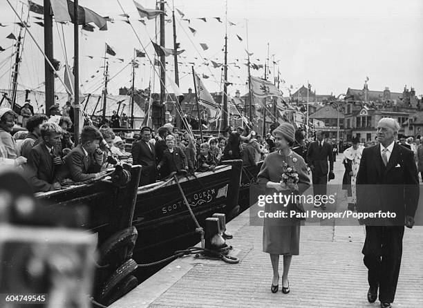 Queen Elizabeth II, followed by the Duke of Edinburgh and Robert Blance , the Provost of Lerwick, walks along the quayside of Lerwick full of packed...