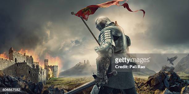 mittelalterlicher ritter mit banner und schwert stehen in der nähe von burning castle - the crusades stock-fotos und bilder