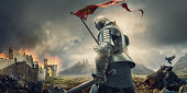Medieval Knight With Banner and Sword Standing Near Burning Castle