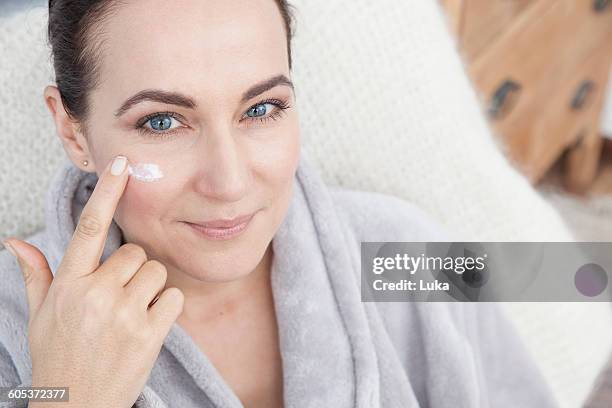 mature woman applying moisturiser to face - produto antienvelhecimento imagens e fotografias de stock