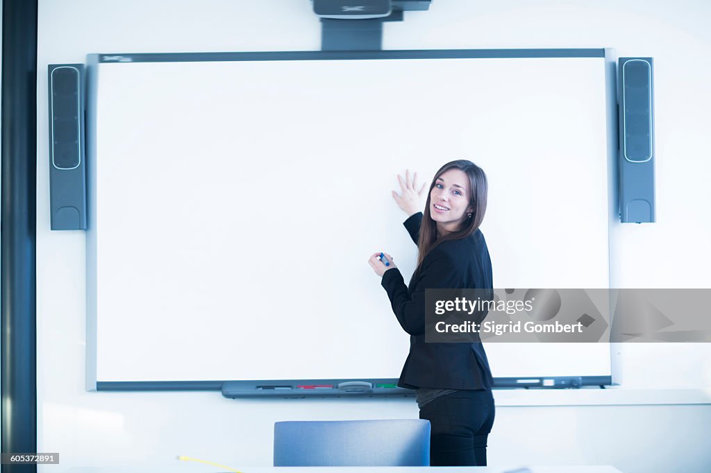 Young woman in office using whiteboard, looking over shoulder at camera smiling