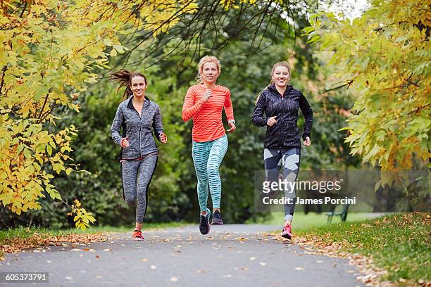 three female runners running along park path - krakow park stock pictures, royalty-free photos & images