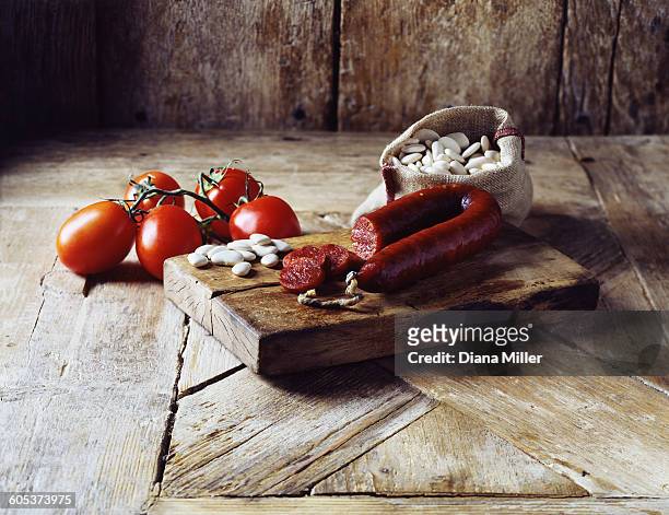 roma tomatoes on the vine, chorizo and butter beans in burlap sack on wooden cutting board - chorizo stockfoto's en -beelden
