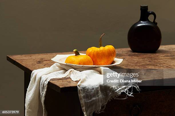 pumpkins in serving dish on table with brown glass bottle - pumpkin still life stock pictures, royalty-free photos & images