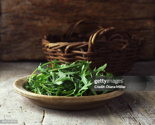 plate of rocket in wooden bowl and wicker basket - arugula stock pictures, royalty-free photos & images