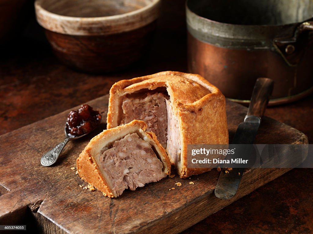 Sliced Melton Mowbray pork pie with spoonful of pickle on wooden cutting board