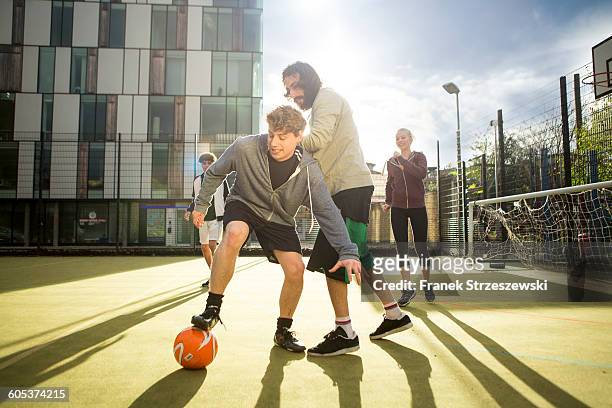 group of adults playing football on urban football pitch - urban football pitch stock pictures, royalty-free photos & images