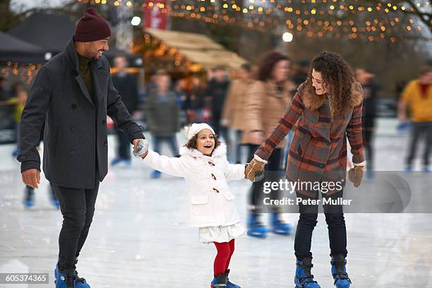 girl holding parents hands ice skating, smiling - patinoire extérieure photos et images de collection