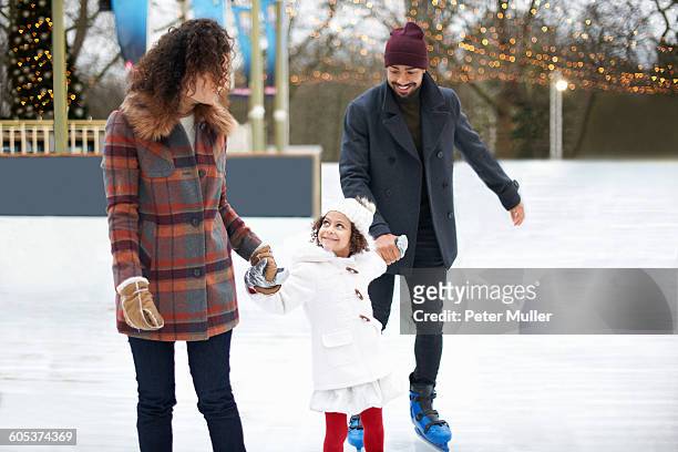 girl ice skating, holding hands with parents looking up smiling - family ice skate stock pictures, royalty-free photos & images