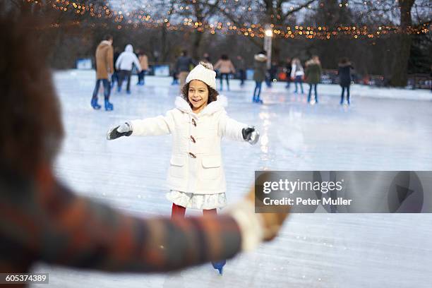 girl on ice rink, arms open skating to mother smiling - family ice skate stock pictures, royalty-free photos & images