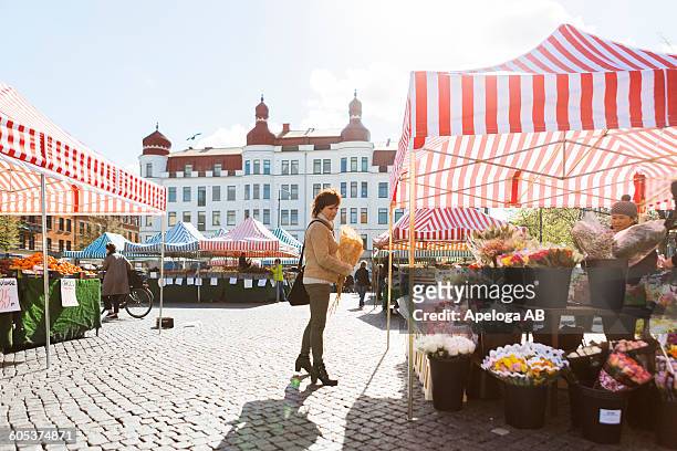 full length side view of woman buying flowers at market stall - stand stock-fotos und bilder