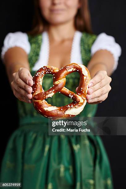 young woman in dirndl holding pretzel - breze stock-fotos und bilder