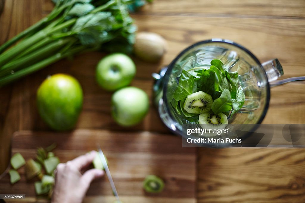 Woman cutting green kiwi on wooden table