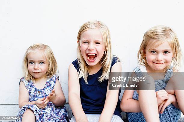 portrait of three young sisters sitting in front of white wall - children only stock-fotos und bilder