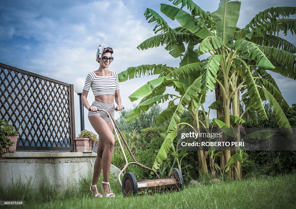 Young stylish woman pushing lawnmower in garden