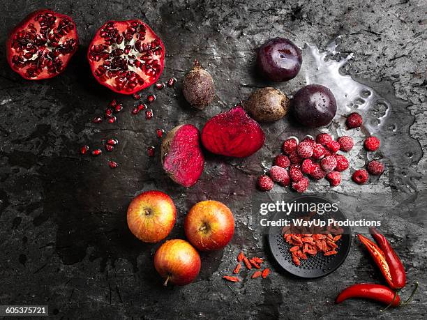 overhead view of halved red fruit and vegetables on dark background - goji berry stock pictures, royalty-free photos & images