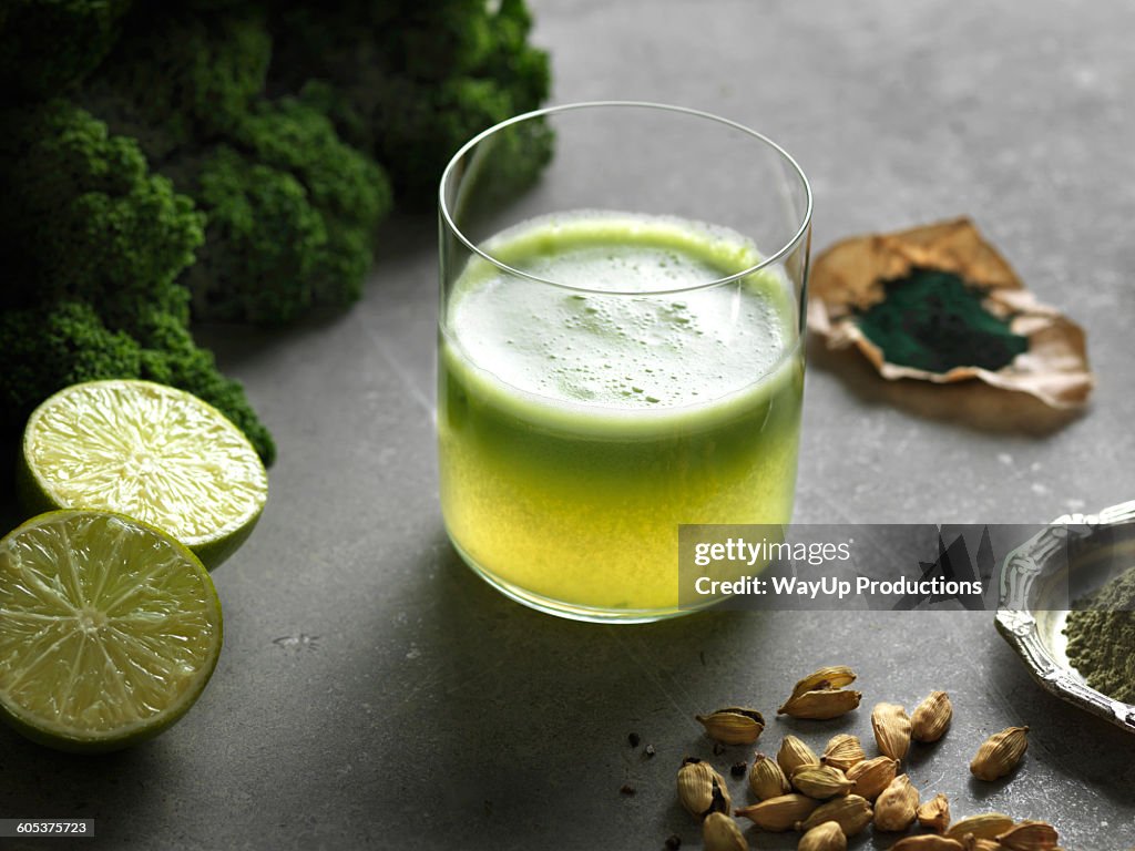 High angle view of green raw juice with halved lime and nutritional supplement