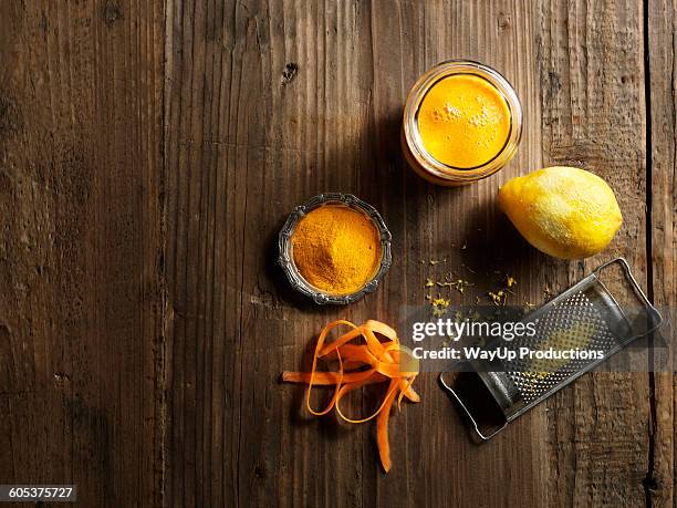 overhead view of yellow raw juice with grated lemon and carrot on wood grain pattern background - orange powder stock pictures, royalty-free photos & images