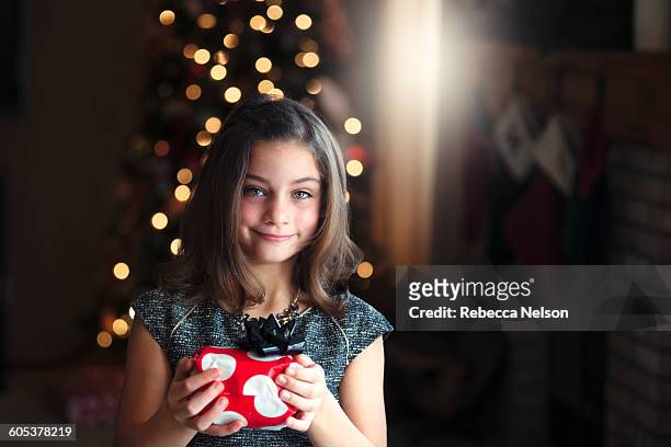 portrait of girl in front of christmas tree holding gift looking at camera smiling - before christmas stock-fotos und bilder