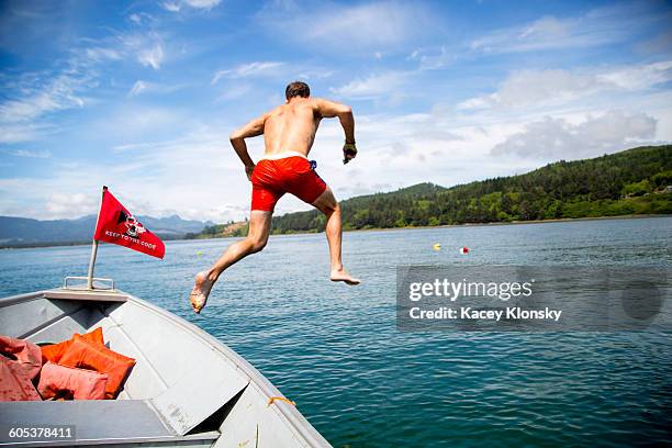 mid adult man jumping into sea from boat, nehalem bay, oregon, usa - zwembroek stockfoto's en -beelden