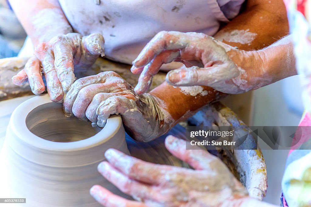 Close up of female potter and mature student hands making pot on potters wheel