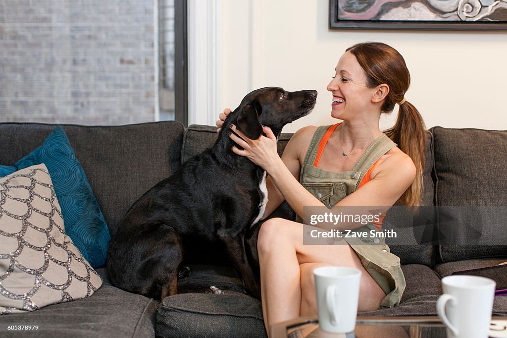 Young woman sitting on sofa face to face with pet dog smiling