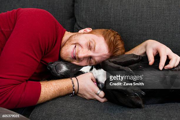 young man lying on sofa hugging pet dog eyes closed smiling - dog eyes closed stock pictures, royalty-free photos & images