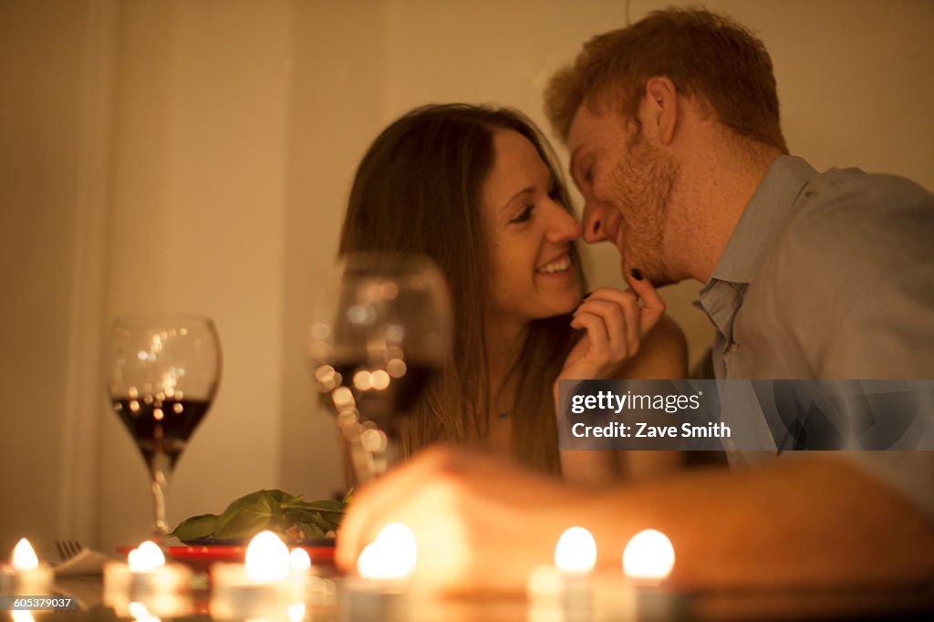 Couple enjoying a glass of red wine by candlelight, face to face smiling