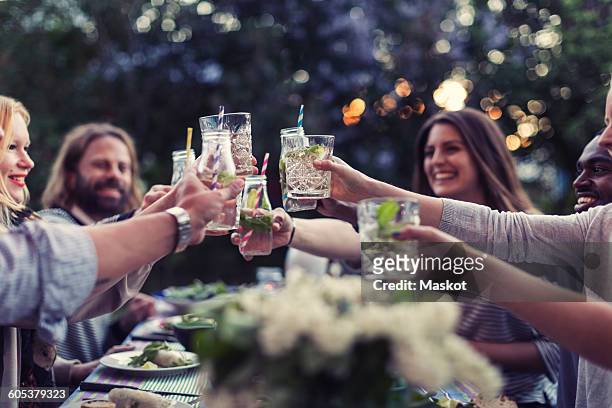 multi-ethnic friends toasting mojito glasses at dinner table in yard - drink stock-fotos und bilder