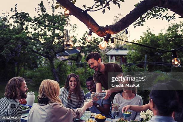 happy man serving water to friend during dinner party at yard - garden party foto e immagini stock