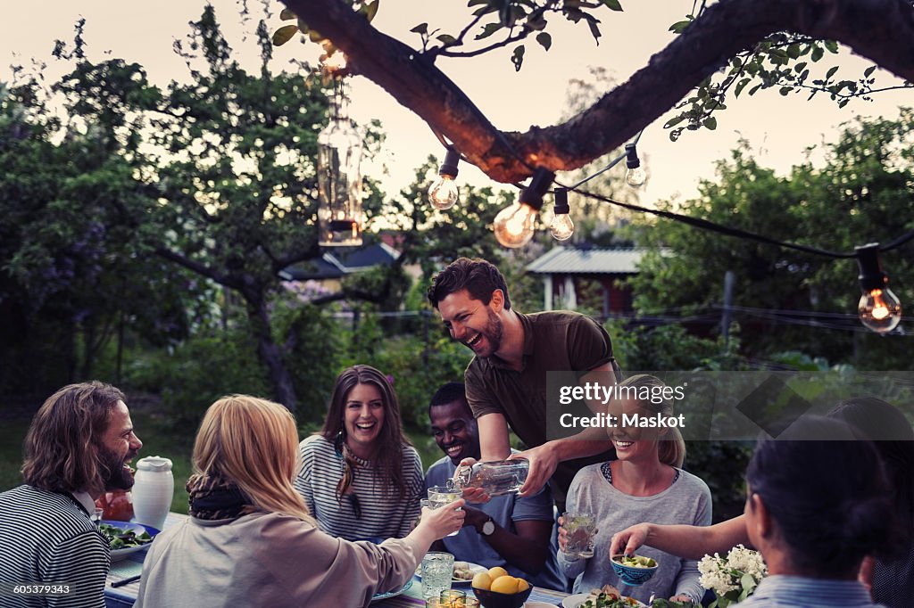 Happy man serving water to friend during dinner party at yard