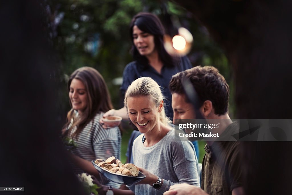 Happy woman holding bread bowl while enjoying dinner party with friends at yard