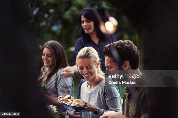happy woman holding bread bowl while enjoying dinner party with friends at yard - evening meal stock pictures, royalty-free photos & images