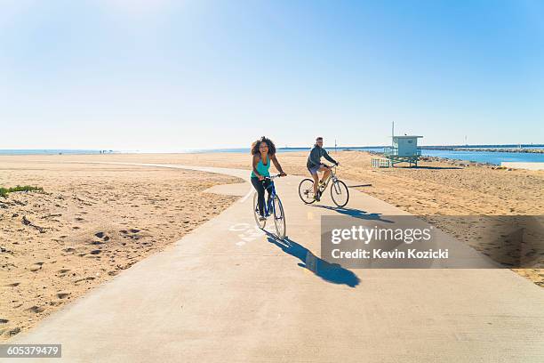 couple cycling along pathway at beach - bike beach stockfoto's en -beelden