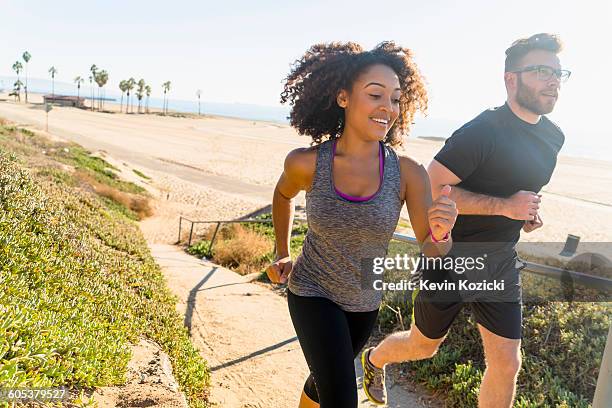 couple running along pathway by beach - woman summer sport outside fotografías e imágenes de stock