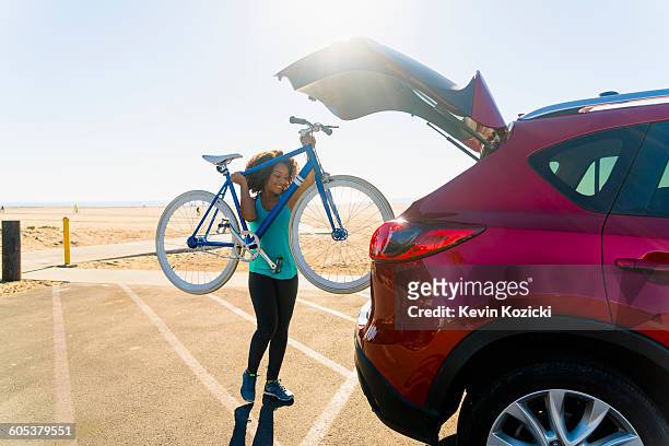 mid adult woman putting bicycle into car boot - auto kofferraum stock-fotos und bilder