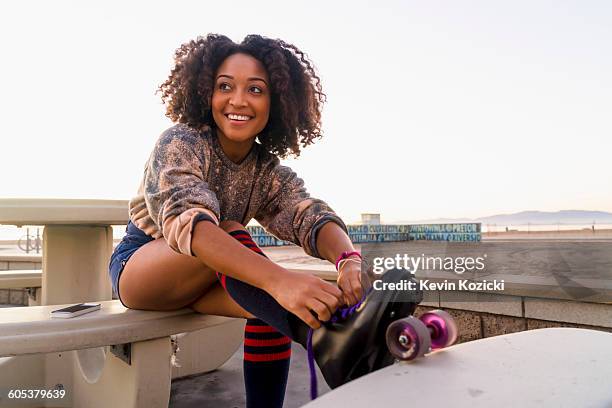 mid adult woman sitting outdoors, tying rollerskates - rollerskates foto e immagini stock