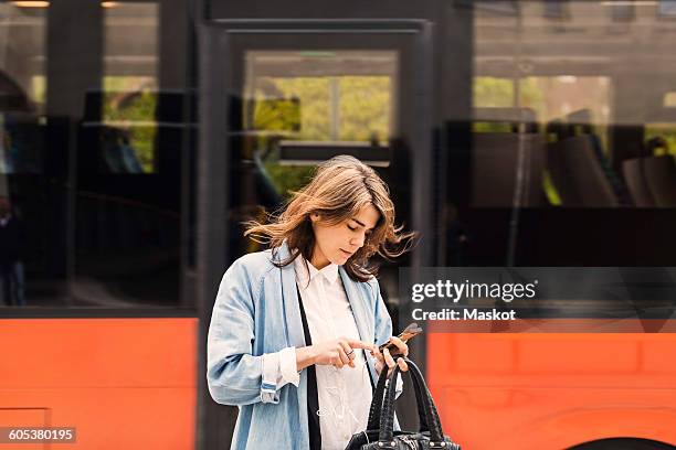 young woman using mobile phone against bus - bushalte stockfoto's en -beelden