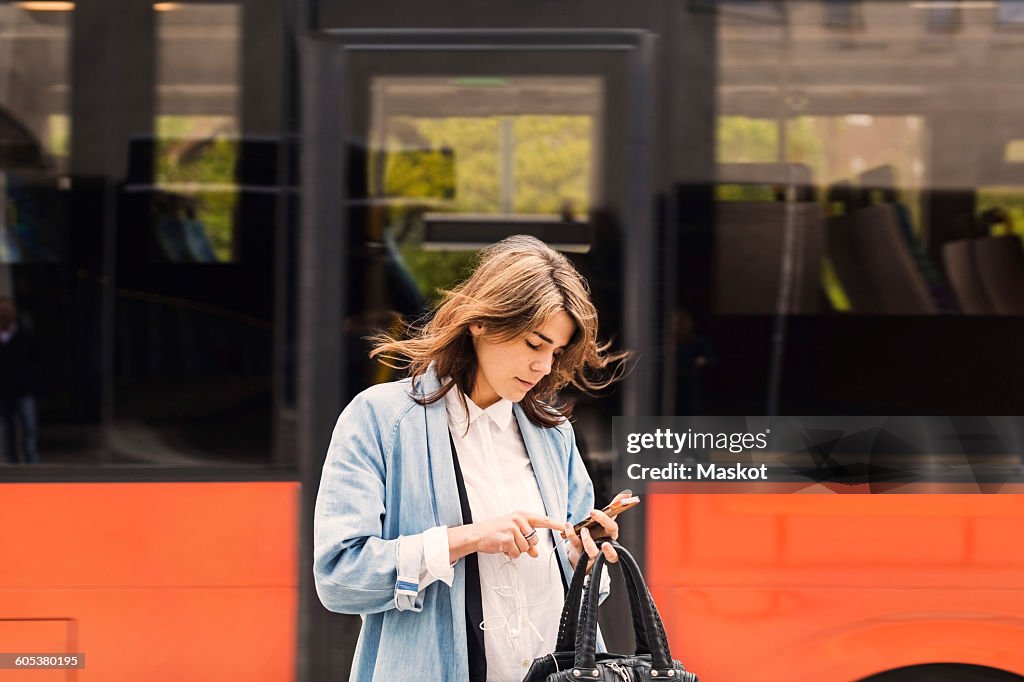 Young woman using mobile phone against bus