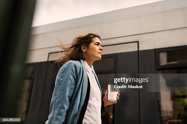 low angle view of young woman holding disposable cup while walking by tram - railroad station stock pictures, royalty-free photos & images