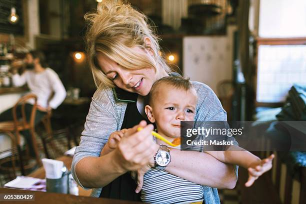 mid adult mother trying to feed baby boy in restaurant - toddler crying stock pictures, royalty-free photos & images