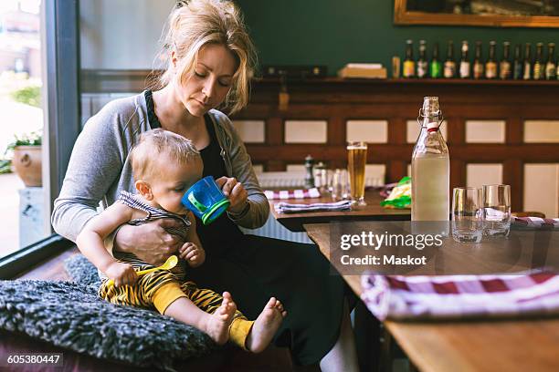 mid adult woman feeding water to son in restaurant - baby cup fotografías e imágenes de stock