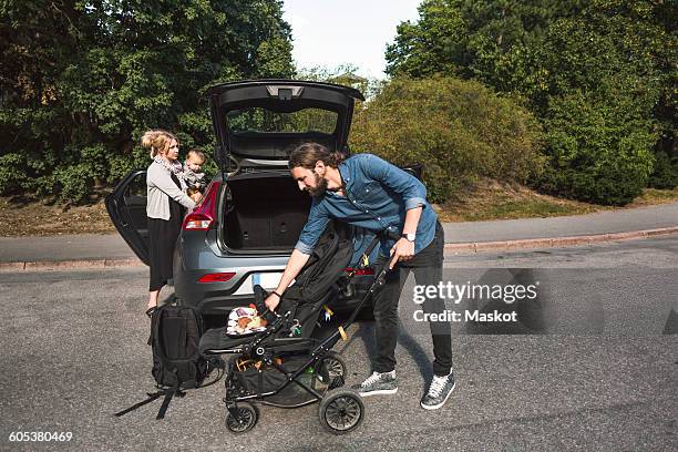 mid adult parents with baby boy and stroller near car on street - stroller stock pictures, royalty-free photos & images