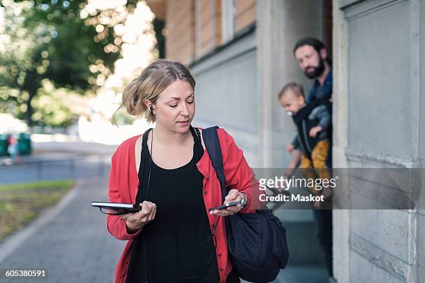 mid adult woman using mobile phone while leaving for work with family in background - leaving home stock pictures, royalty-free photos & images