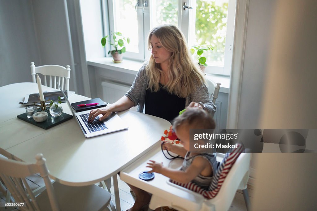 Mid adult woman using laptop while taking care of baby boy at home
